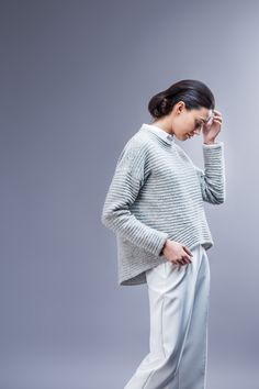 a woman standing in front of a gray background talking on a cell phone and holding her hand to her ear