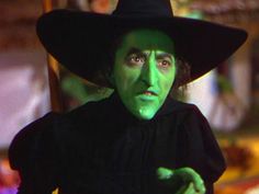 a man in a witches costume with green paint on his face and hands, pointing to the side