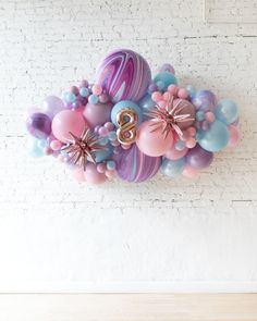 balloons are arranged in the shape of numbers on a white brick wall with pink, blue and purple colors