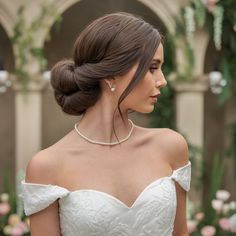 a woman wearing a white wedding dress with a pearl necklace on her neck and pearls in her hair