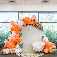 an orange and white balloon arch is set up in the middle of a room with chairs