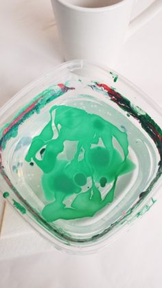 a white cup sitting on top of a table filled with green liquid and paint covered dishes