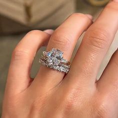 a close up of a person's hand with two engagement rings on their fingers