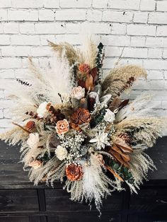 an arrangement of dried flowers and foliage on a table in front of a brick wall