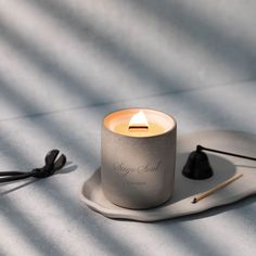 a lit candle sitting on top of a plate next to a pair of scissors and thread