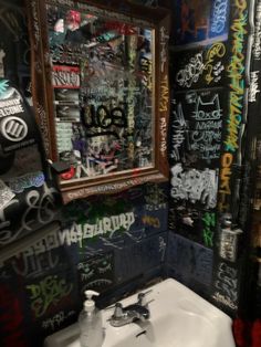 a bathroom with graffiti on the walls and a mirror above it that has spray paint all over it