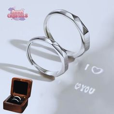 two wedding rings sitting on top of a table next to an open ring box with the word i love you