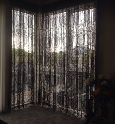 an open window with black sheer curtains in the corner and flowers on the floor next to it