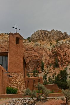 an adobe church with a cross on the roof and mountains in the back ground behind it