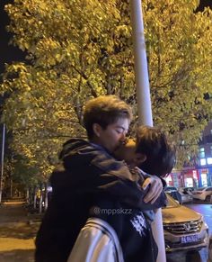 two men hugging each other on the street corner at night with trees and buildings in the background