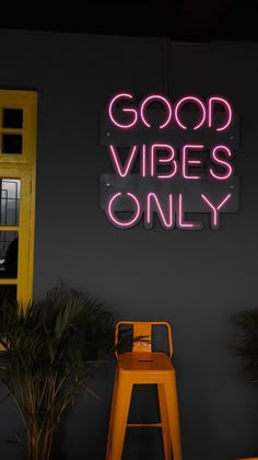 a neon sign that says good vibes only on the wall next to a yellow chair