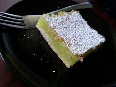 a piece of cake with powdered sugar on top sits on a black plate next to a fork