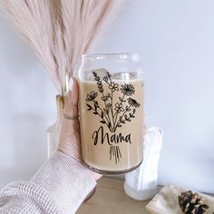 a person holding a glass with flowers on it and the words mama written in black