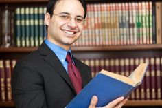 a man in a suit and tie holding a blue book with bookshelves behind him