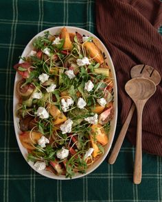 a white bowl filled with salad next to a wooden spoon on top of a green table cloth