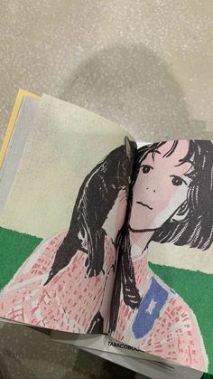 an open book with a drawing of a woman's face on the cover and green grass in the background