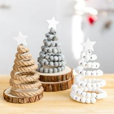 three small christmas trees made out of rope and beads on a wooden table in front of a white wall