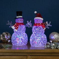 two snowmen with hats and scarfs on top of a table next to christmas decorations