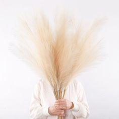 a person holding a bunch of dry grass in front of their face with both hands