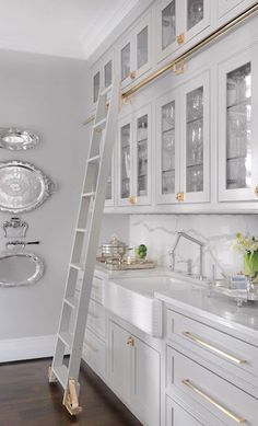 a ladder is in the middle of a kitchen with white cabinets and gold trimmings