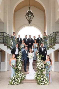 a group of people in formal wear posing for a photo on some steps with flowers and greenery