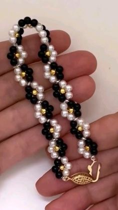 a woman's hand is holding a beaded necklace with black, white and gold beads