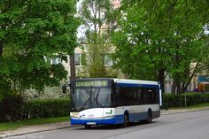 a blue and white bus driving down a street next to tall buildings with trees on both sides