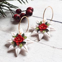 two white star shaped earrings with red flowers and green leaves on them next to berries