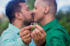 two men are kissing each other with their wedding rings in front of them and the man is wearing a green shirt