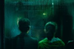 three people standing in front of a window with rain drops on the glass and one person wearing a green shirt