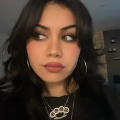 a woman with long black hair and large hoop earrings on her neck looking at the camera