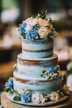 a three tiered cake with blue and white flowers on the top is sitting on a wooden table