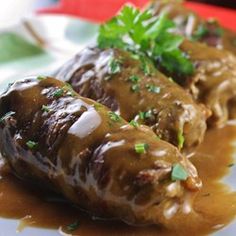 two meat rolls covered in gravy and garnished with parsley on a white plate