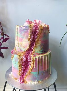 a multi - layer cake with pink and gold icing on top, sitting on a table