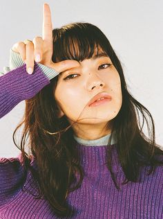 a woman with long hair holding her hand up to the side while wearing a purple sweater