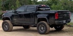 a black truck is parked on the side of a road near water and trees in the background