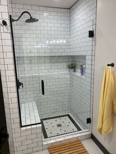 a walk in shower sitting next to a white tiled wall and wooden bench with yellow towels on it