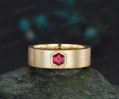 a gold ring with a red stone in the center on top of a green rock