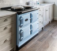 a blue stove top oven sitting inside of a kitchen next to white cabinets and drawers