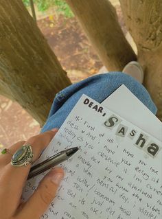 someone holding a note and pen in their hand while sitting under a tree with the words dear, saha written on it