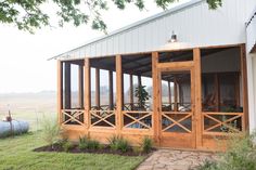 a wooden porch sitting next to a white building on top of a lush green field