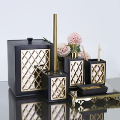 four pieces of black and gold bathroom accessories with flowers in vases next to them