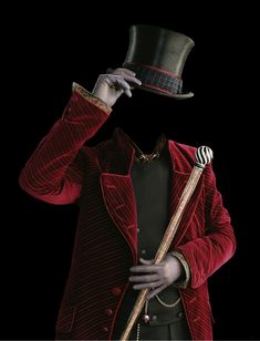 a man in a red suit and top hat holding a cane to his face with one hand