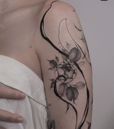 a woman's arm with flowers and vines tattoo on her left shoulder, next to a white shirt