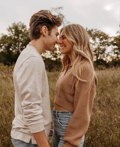 a young man and woman are standing together in the grass looking into each other's eyes