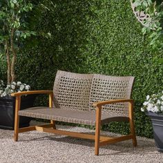 a wooden bench sitting in front of a green wall covered with plants and pillows on top of it