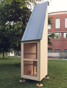 a small wooden structure sitting on top of a lush green field next to a tall red brick building