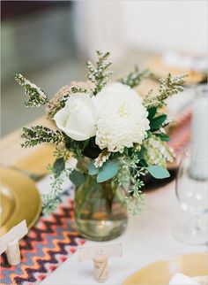 a vase filled with white flowers sitting on top of a table next to plates and glasses