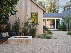 an outdoor fire pit in the middle of a gravel area next to a wooden building