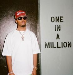 a man wearing sunglasses and a red hat standing in front of a sign that says one in a million